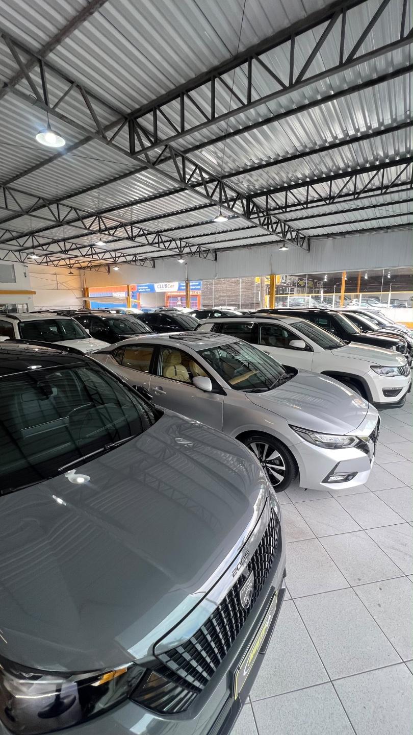 Showroom coberto de loja de seminovos com carros enfileirados sobre piso claro, com um SUV cinza em primeiro plano ao lado de um sedã prata e de um SUV branco