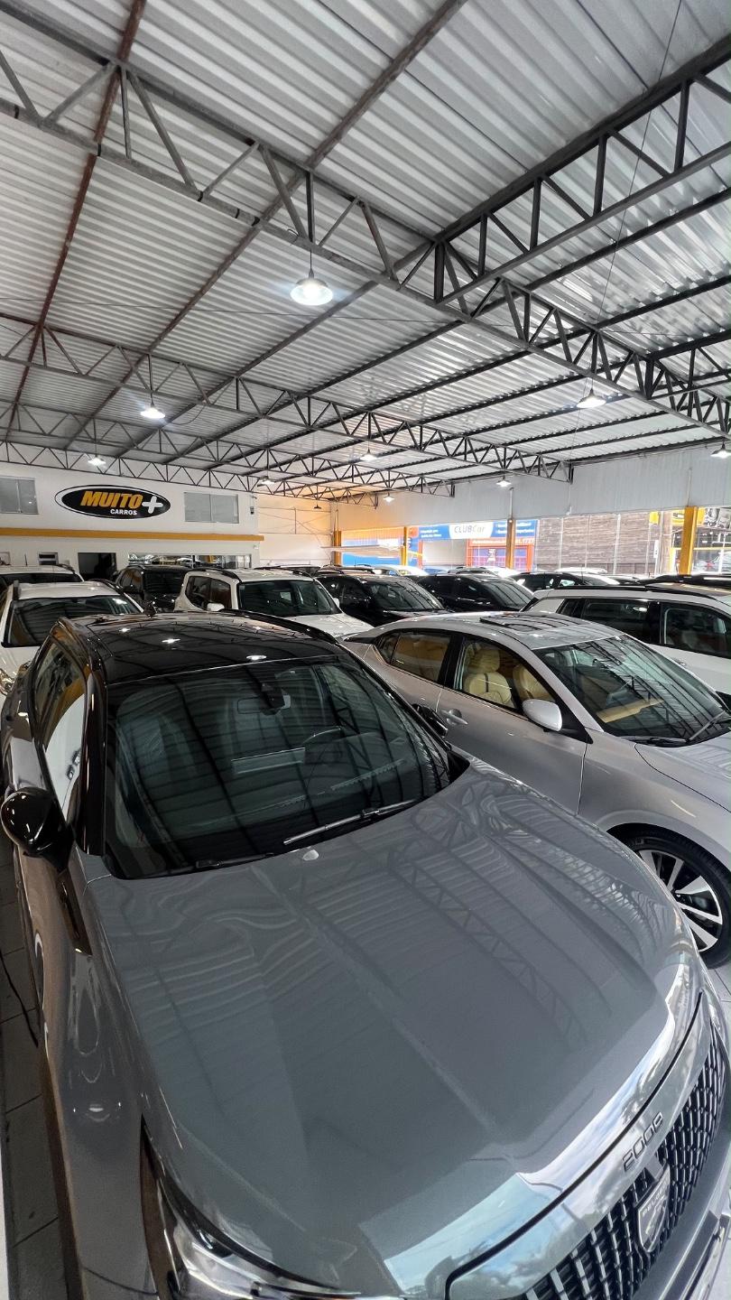 Galpão coberto da Muito Mais Carros com seminovos lado a lado, com destaque para a frente de um SUV cinza com teto preto e inscrição 2008 na grade
