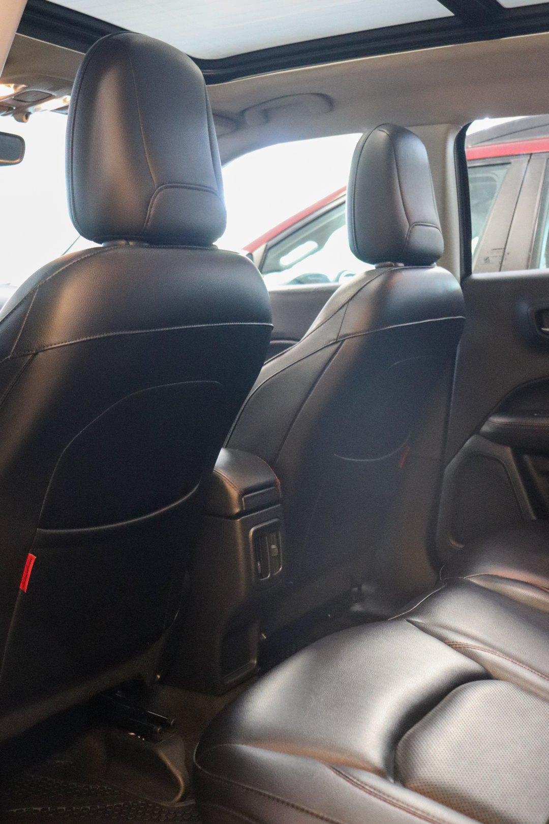 Vista do banco traseiro de um carro com bancos de couro preto e costura vermelha, console traseiro com saídas de ar e teto solar panorâmico