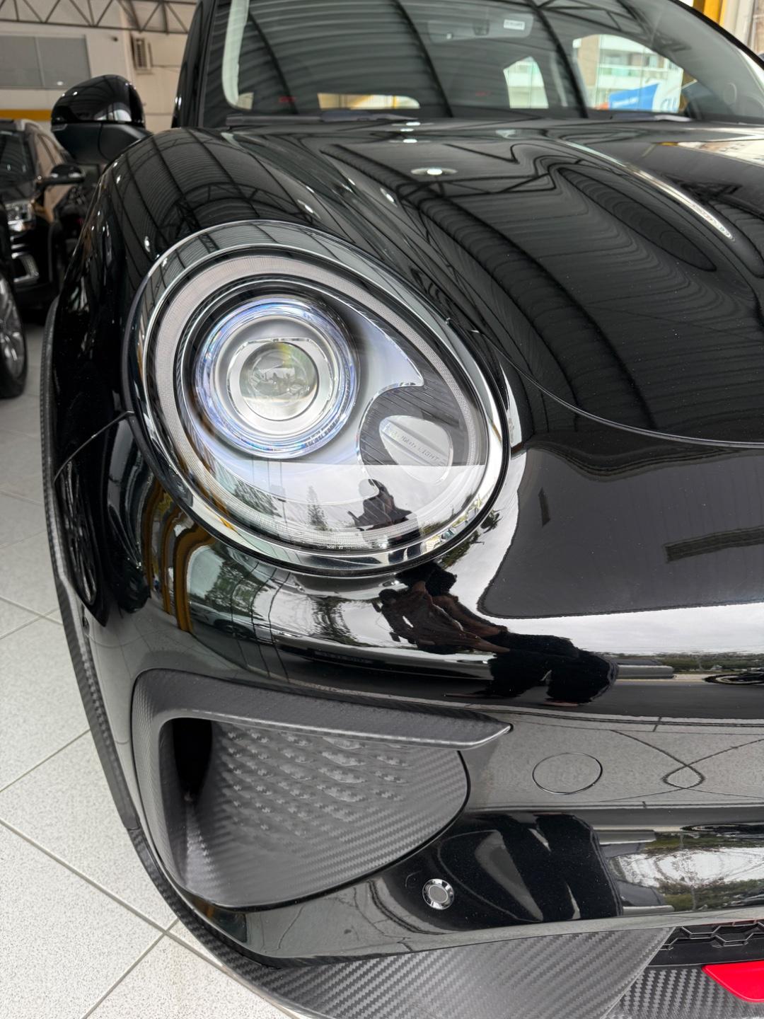 Close da dianteira de um carro preto no showroom, com farol redondo com anel de LED, capô brilhante e para-choque com acabamento que imita fibra de carbono