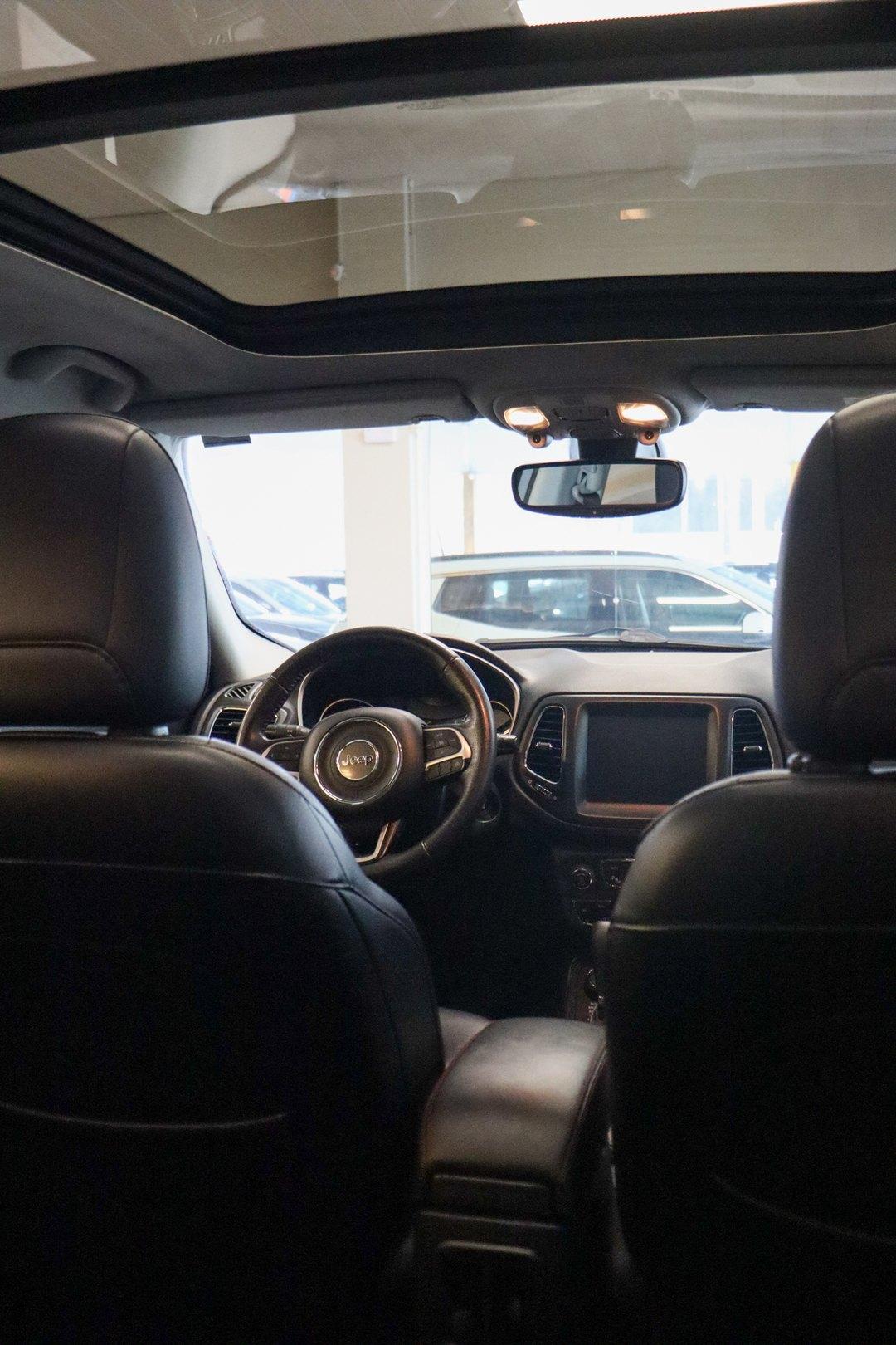 Interior de um SUV Jeep visto do banco de trás, com bancos de couro, central multimídia e teto solar panorâmico