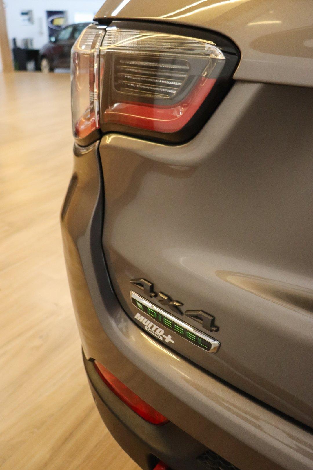 Traseira de um SUV cinza no showroom, com lanterna traseira, emblemas 4x4 e Diesel e adesivo da Muito Mais Carros na tampa