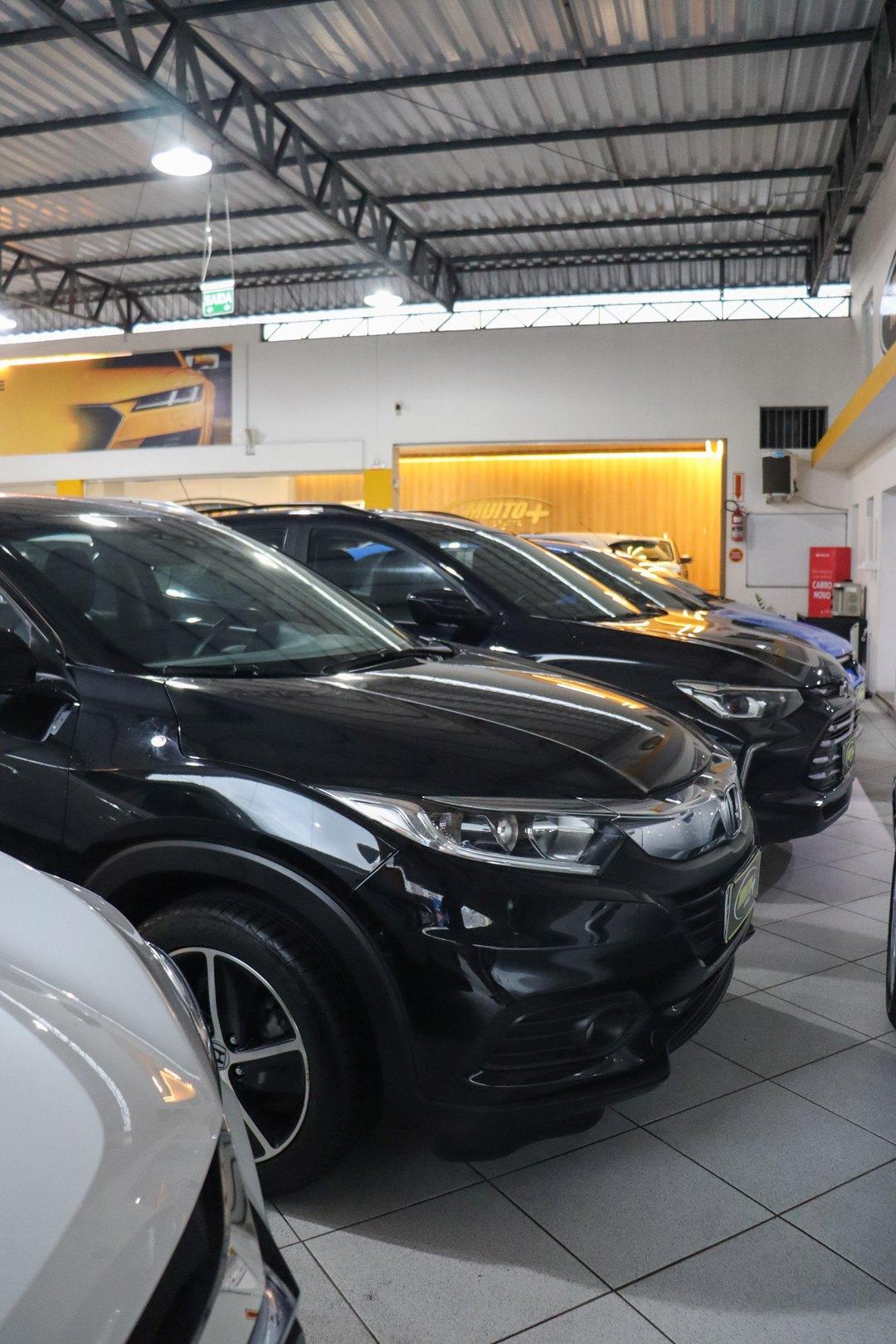 Fileira de SUVs seminovos lado a lado no salão coberto da Muito Mais Carros, com um SUV Honda preto em primeiro plano